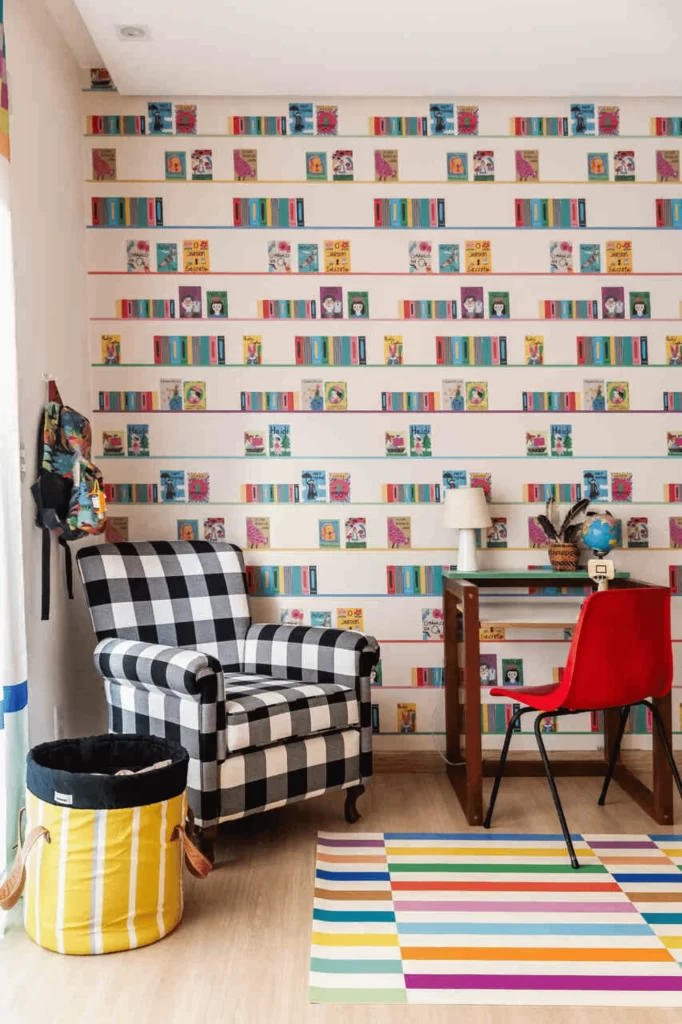 Quarto infantil com poltrona xadrez, escrivaninha, cadeira vermelha e parede decorada com livros, formando um cantinho de leitura aconchegante.