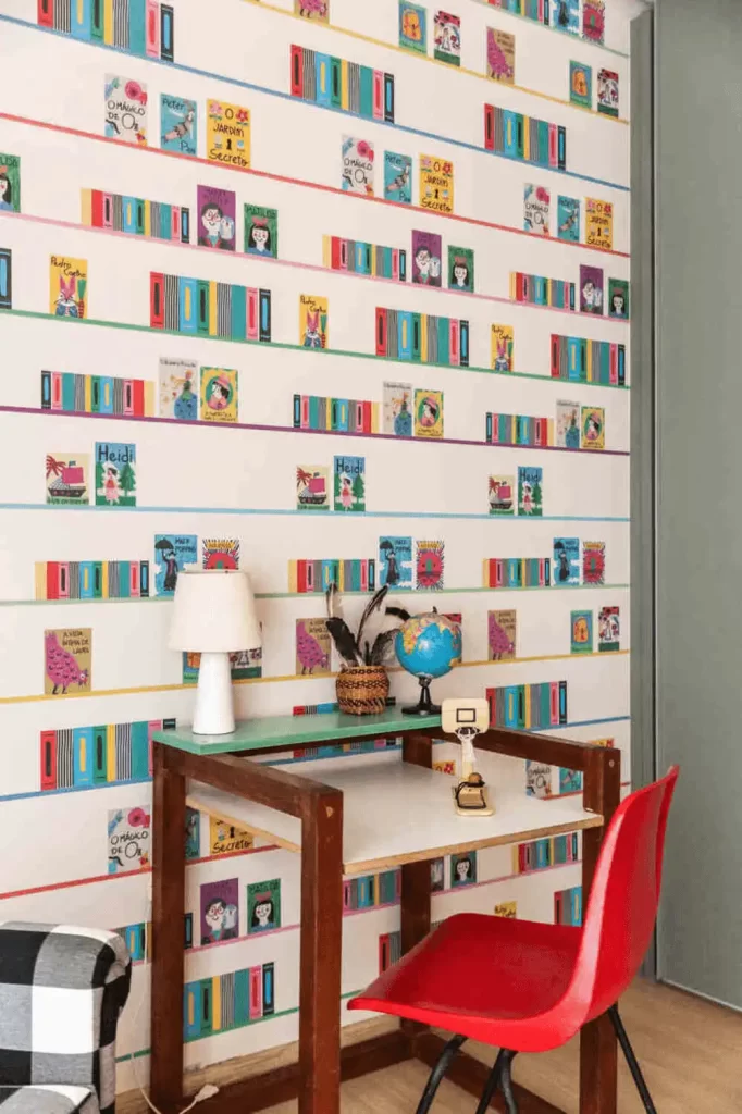 Cantinho da leitura com escrivaninha de madeira, globo terrestre e parede decorada com papel de livros coloridos.