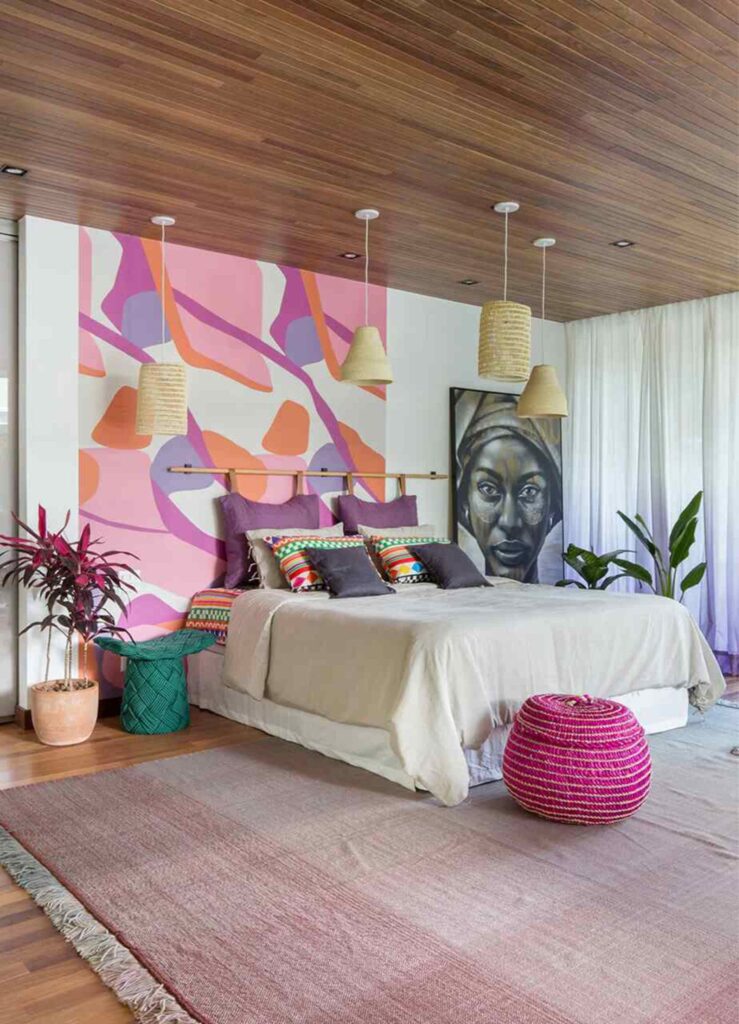 Quarto com parede pintada em tons de rosa e lilás, luminárias de palha e almofadas coloridas, decoração moderna com toque artístico.