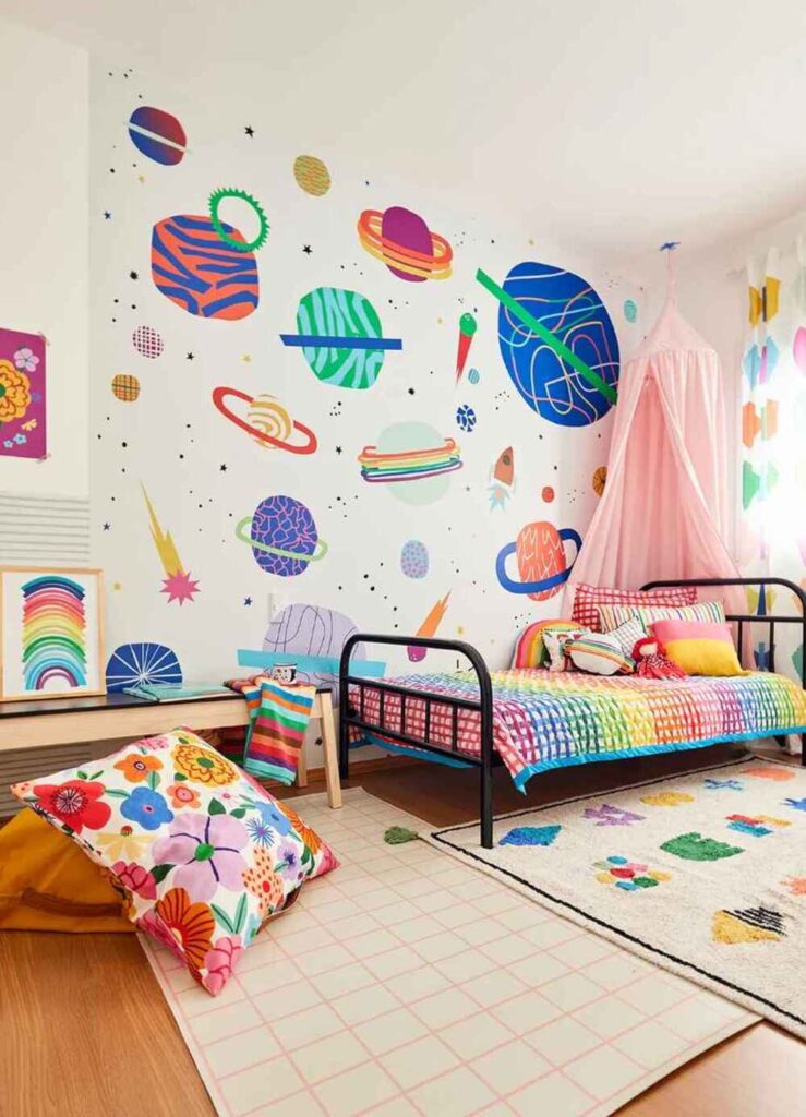 Quarto com parede pintada em tons de rosa e lilás, luminárias de palha e almofadas coloridas, decoração moderna com toque artístico.