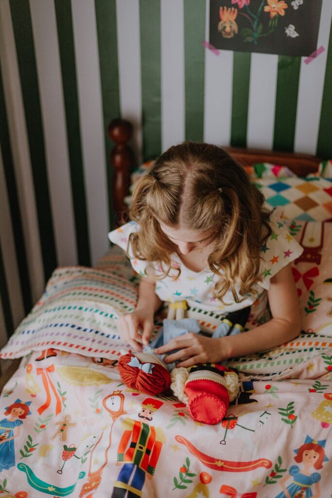 Menina mexendo em bonecas de pano de natal sentada em cama