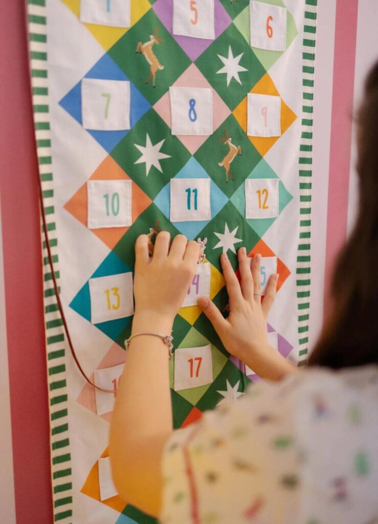 Criança brincando com calendário do Advento natalino de fundo verde com números coloridos.