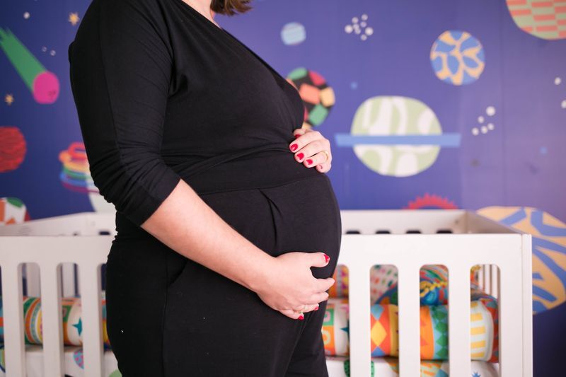 Gestante com mão na barriga em quarto infantil decorado