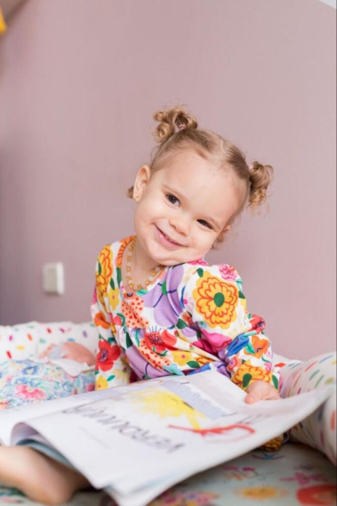 Menina sentada sorrindo e segurando livro infantil