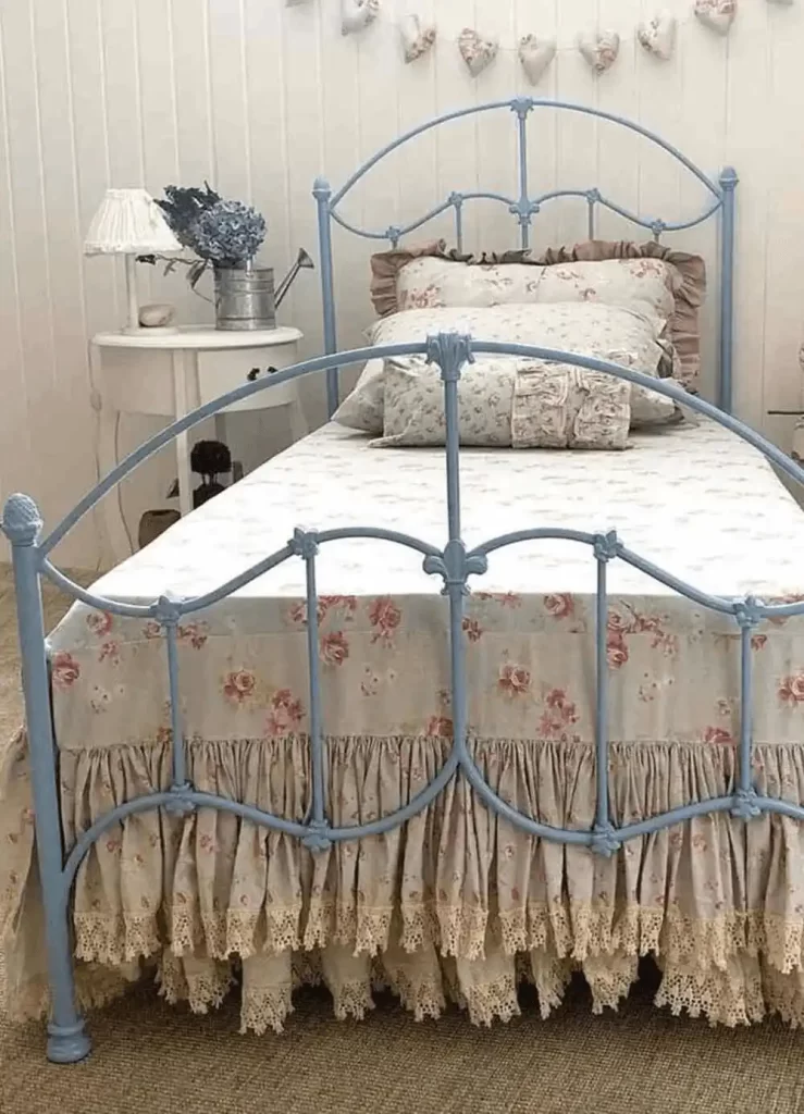 Cama de ferro azul clara com roupa de cama floral e estilo romântico vintage.