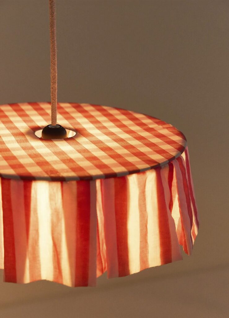 Luminária pendente com tecido xadrez vermelho e bege iluminando quarto infantil.