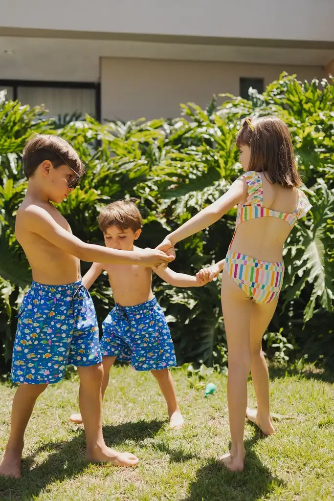 crianças brincando de roda no gramado, usando roupas de banho coloridas e coordenadas da Mooui