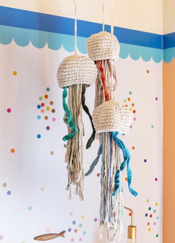 Móbile artesanal de crochê com formato de águas-vivas coloridas penduradas em quarto infantil.
