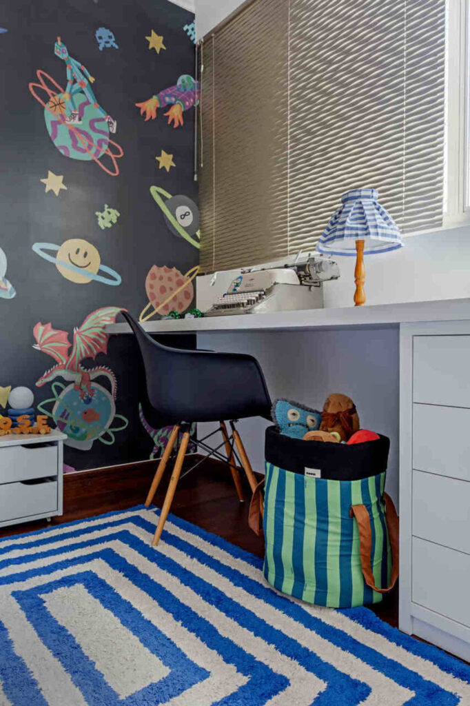 Quarto infantil masculino com tema espaço, escrivaninha e tapete geométrico azul.