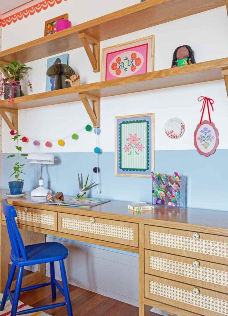 Escrivaninha infantil e prateleiras de madeira em espaço de estudo com decoração delicada.