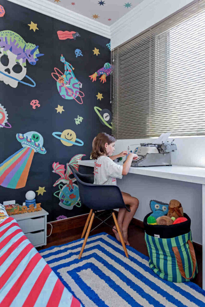 Escrivaninha infantil em quarto com tema espaço e parede decorada com planetas.