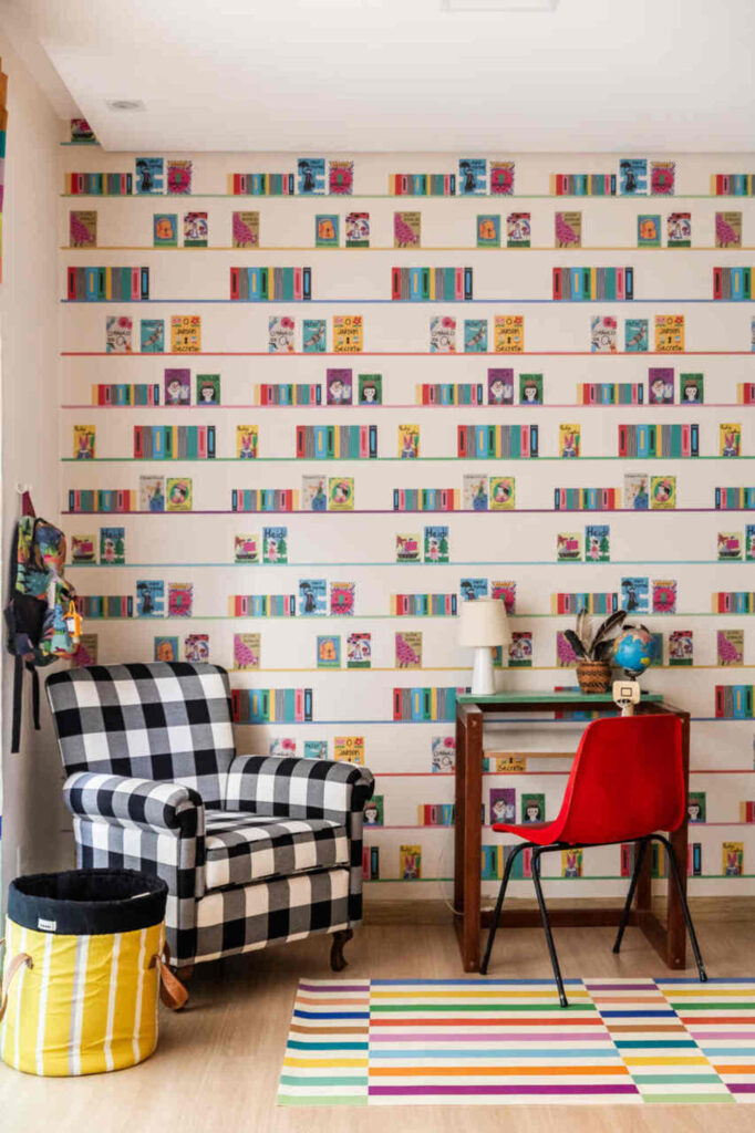Quarto infantil com canto de leitura, poltrona xadrez e parede temática de livros.