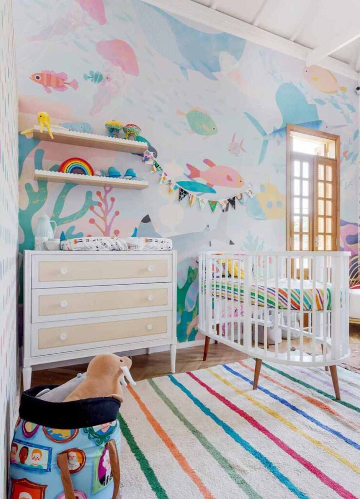 Quarto infantil com tema oceano, mural colorido e berço moderno, ideal para decoração de maternidade criativa.