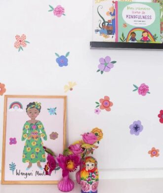 Decoração infantil com adesivos de flores coloridas aplicados em parede branca com livros e objetos decorativos.