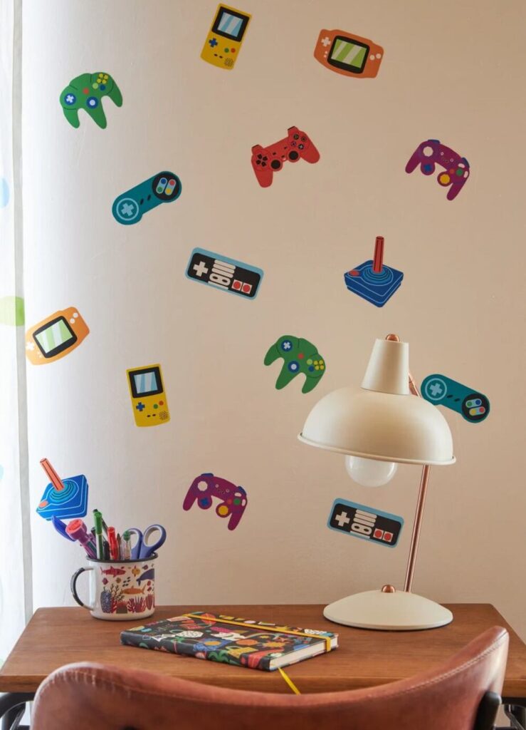 Adesivos de parede infantil com tema videogame e controles retrô decorando quarto e espaço de estudos infantil.