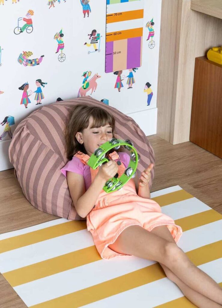 Criança brincando com instrumento musical infantil em ambiente de desenvolvimento sensorial.