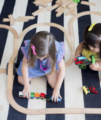 Crianças brincando com trilhos de trem de madeira em atividade lúdica de aprendizado infantil.