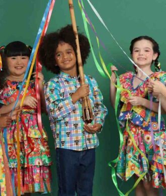 Crianças usando roupas coloridas de São João com fitas e estampas tradicionais em ensaio junino.