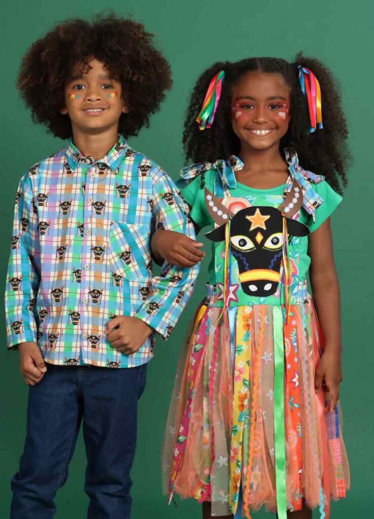 Produção infantil temática Bumba Meu Boi com vestido colorido, fitas e elementos típicos juninos.