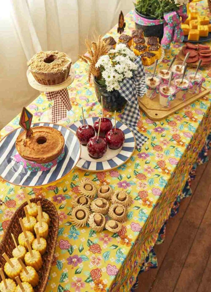 Mesa decorada de arraial com doces típicos, estampas florais coloridas e decoração temática junina.