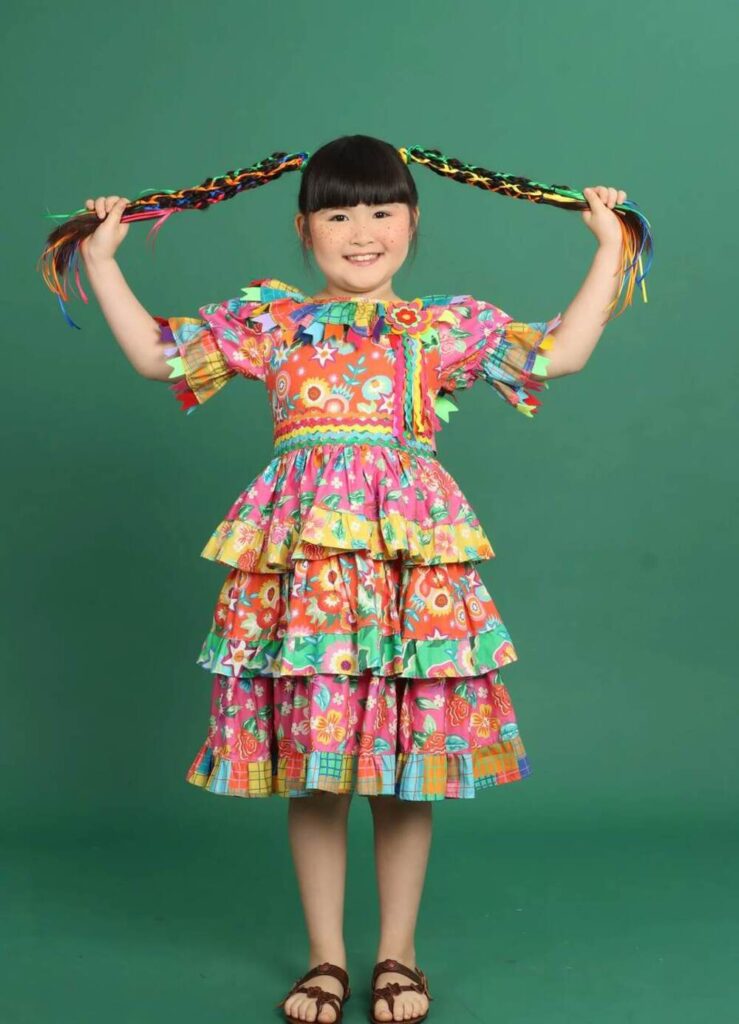 Look festa junina infantil com vestido colorido de chitas, camadas em babados e fitas no cabelo para arraial infantil.