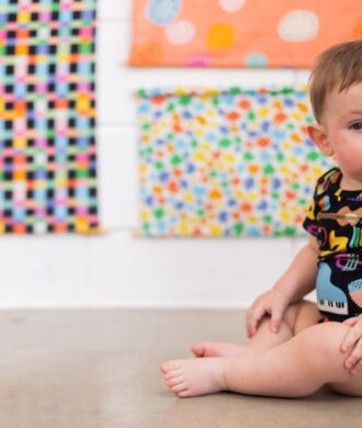 Bebê sentado usando body estampado colorido, uma opção confortável para o enxoval e a saída da maternidade.