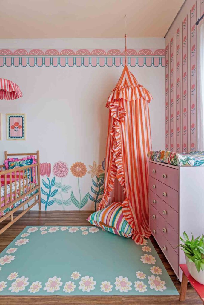 Tapete infantil verde com borda floral em quarto de bebê decorado com dossel listrado e móveis em tons de rosa.